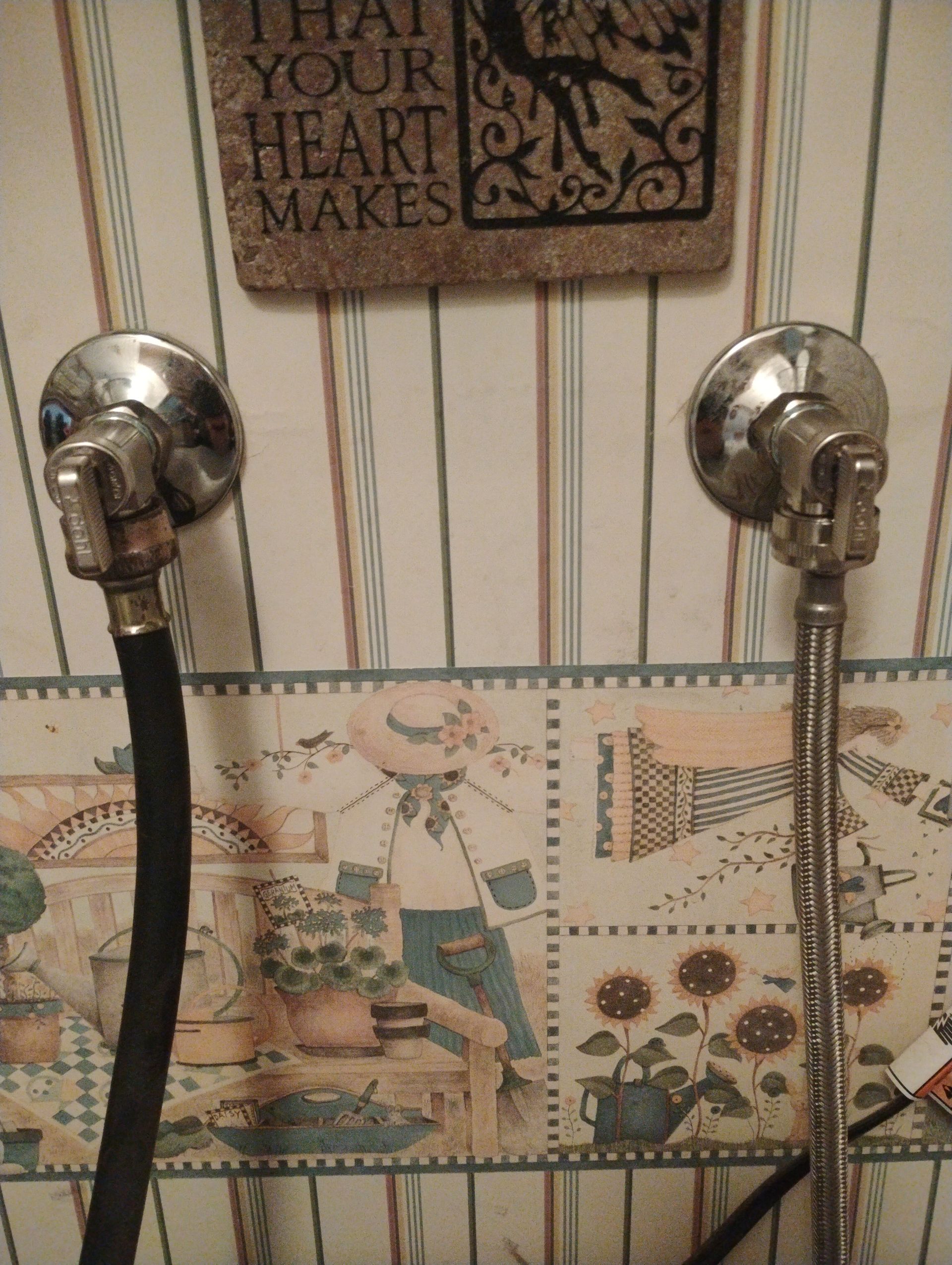 Two chrome shower sprayers hanging on a striped and patterned bathroom wall