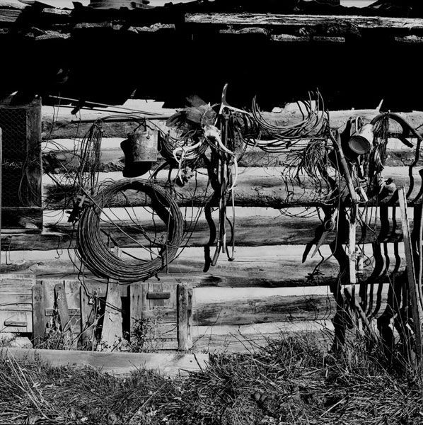 Rustic wooden wall with coiled wire, tools, and weathered objects, outdoors in black and white.