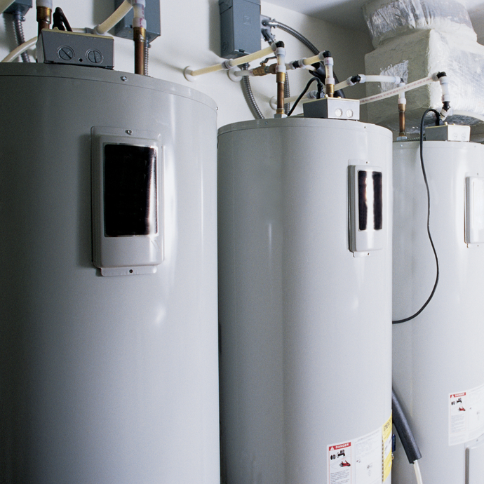 Three white water heaters are lined up in a room