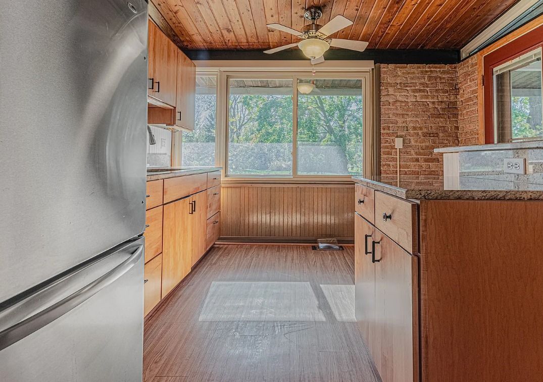Kitchen with wooden cabinets, brick wall, and a large window looking outdoors.