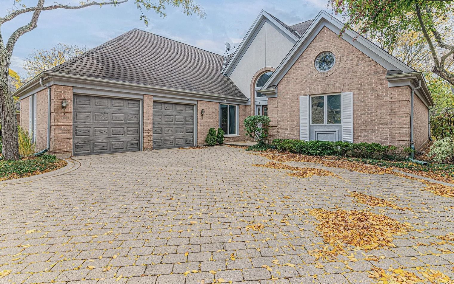 Brick home with a two-car garage, brick paver driveway, and autumn leaves.