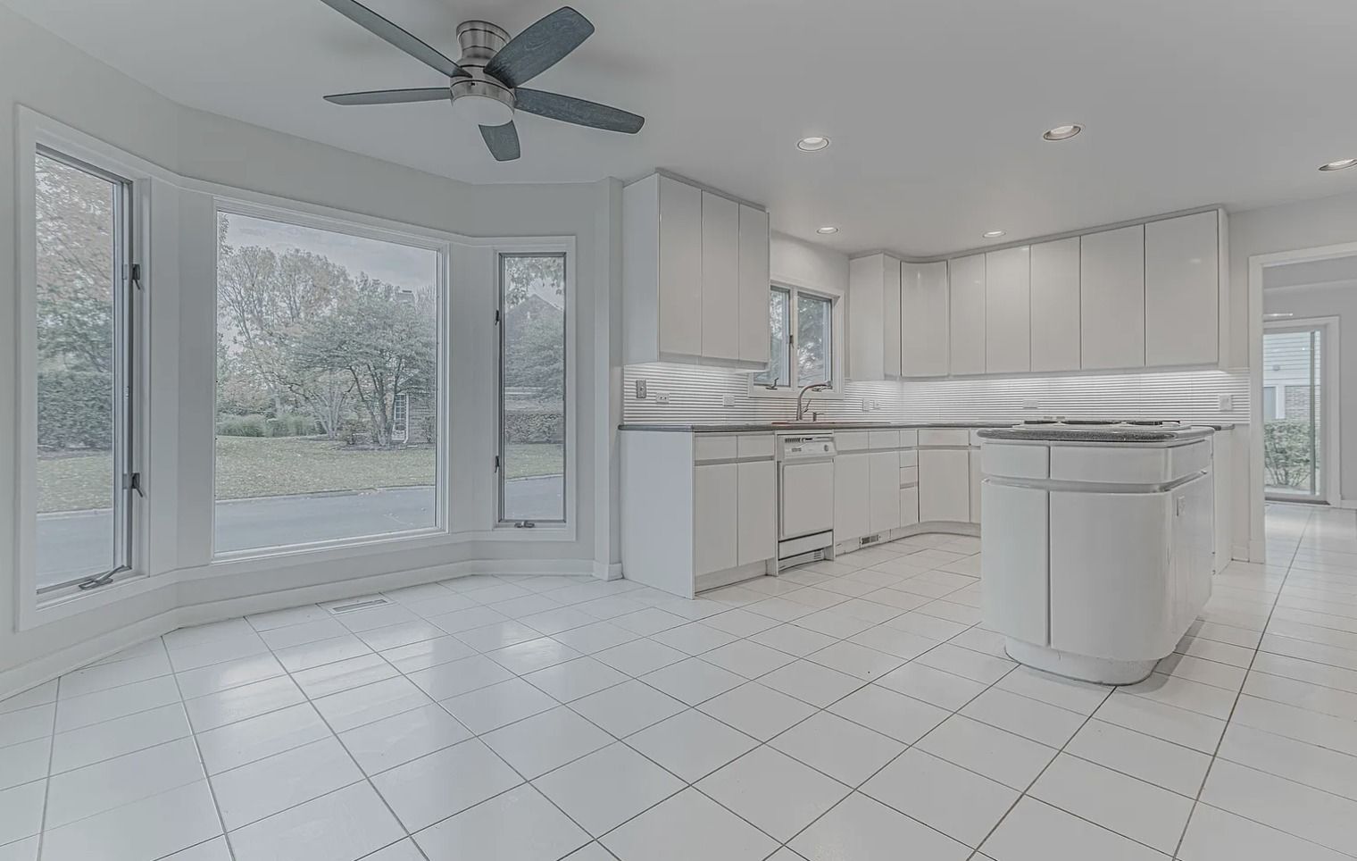 White kitchen with tile floor, cabinets, and island. Bay windows look out to exterior.