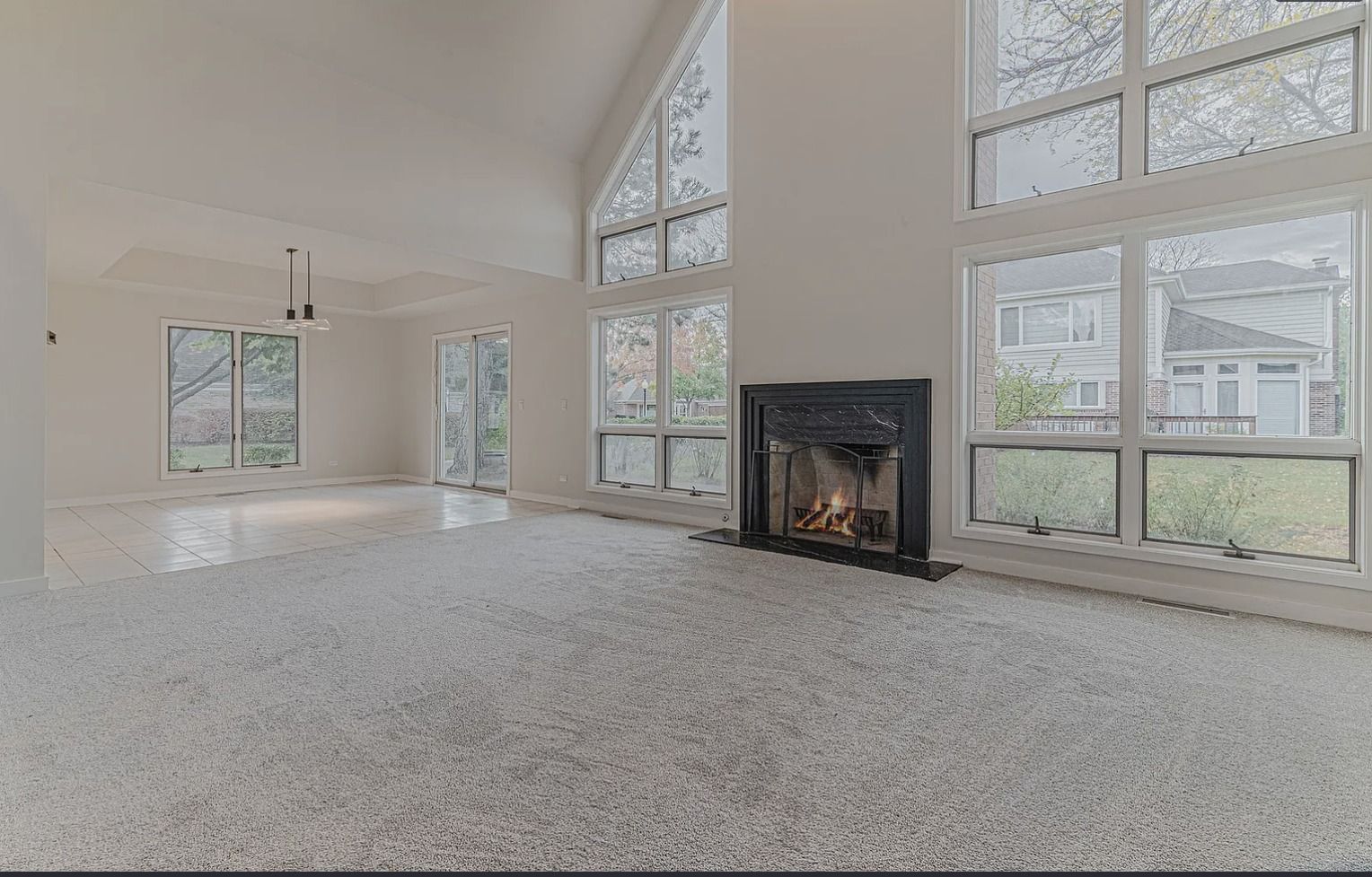 Empty living room with white carpet, fireplace, and large windows.