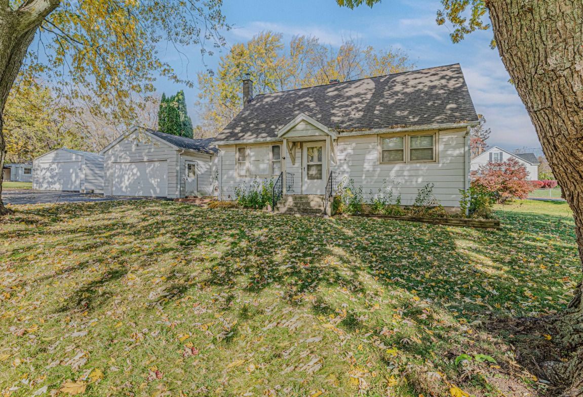 White house with attached garage, surrounded by trees and autumn leaves on a sunny day.