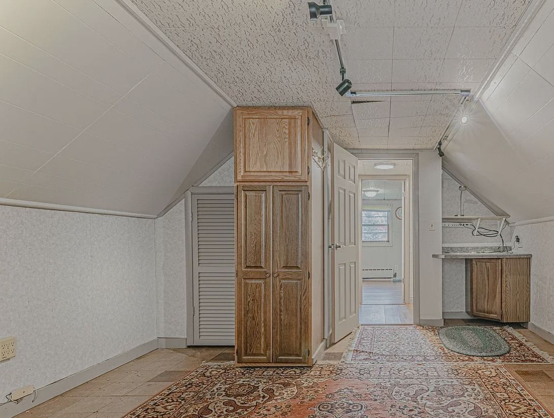 Attic room with sloped ceilings, cabinets, a rug, and a doorway leading to another room.