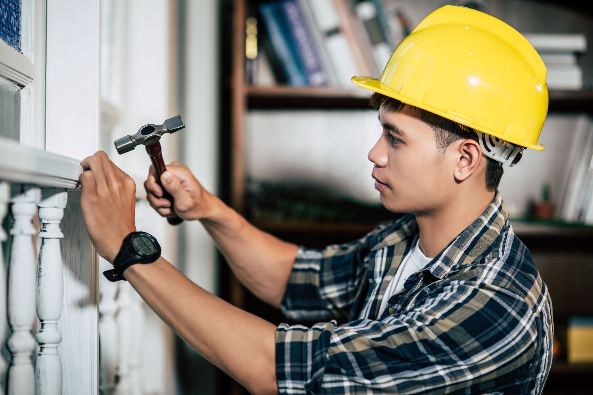 Person in yellow hard hat hammers a white molding.