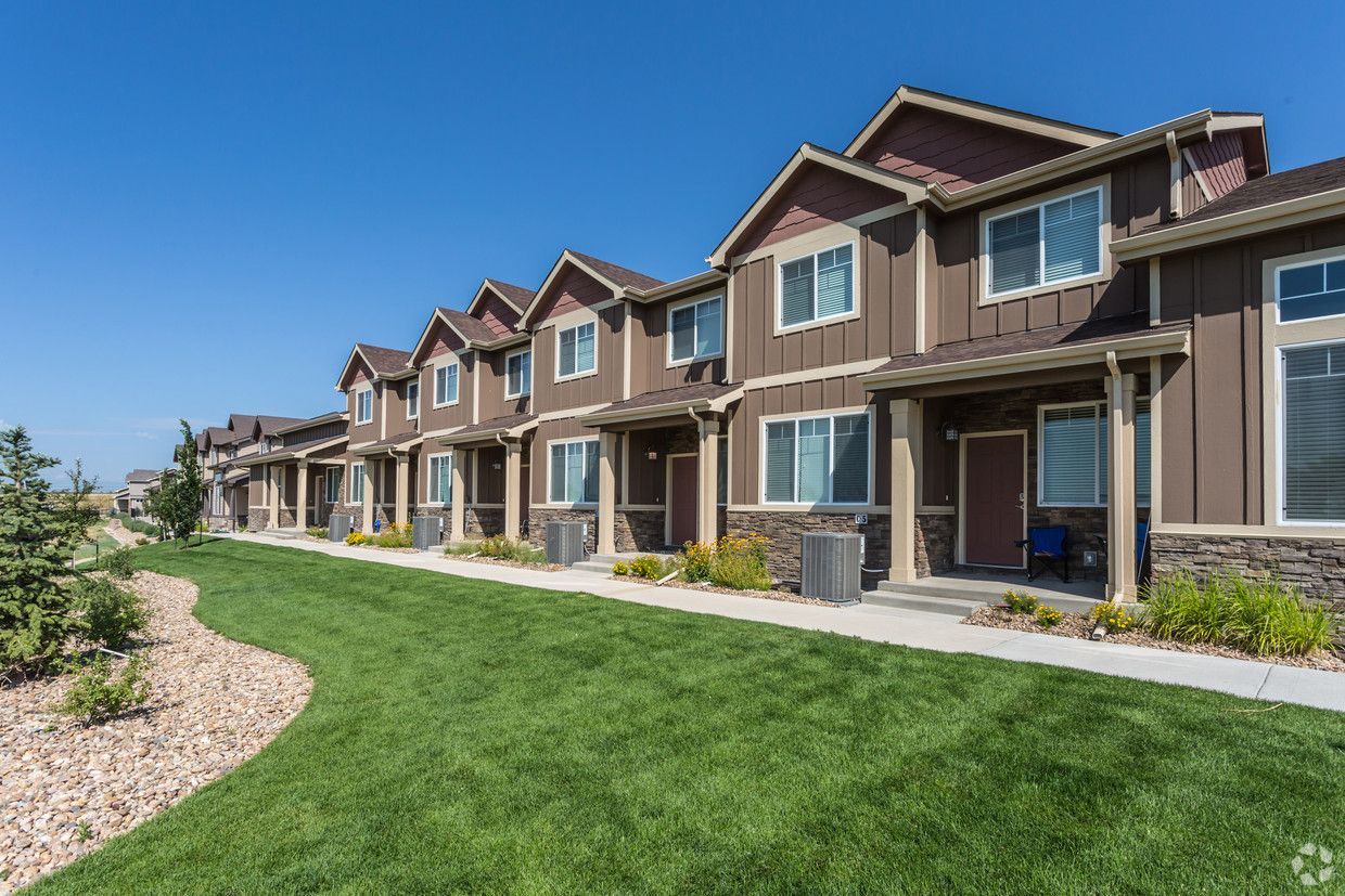 Row of brown townhouses with green lawns and blue sky.