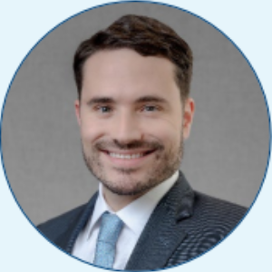 A smiling professional wearing a suit and light blue tie against a gray background, enclosed in a circular frame.