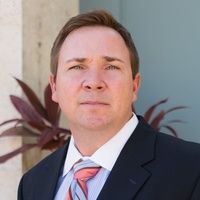 A man in a suit and tie is standing in front of a plant.