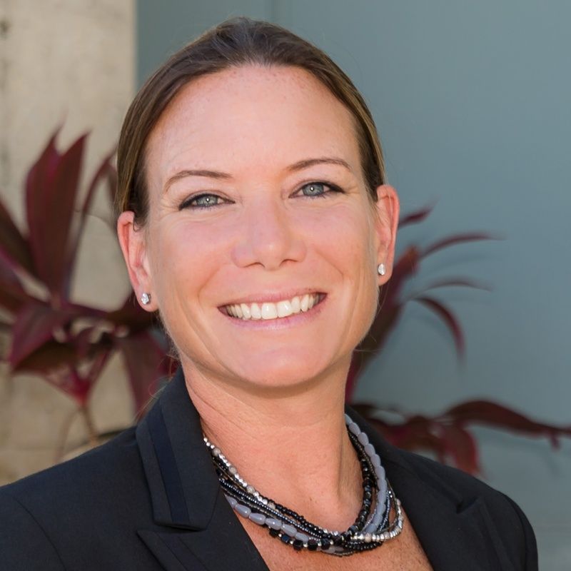 A woman wearing a black jacket and a necklace smiles for the camera