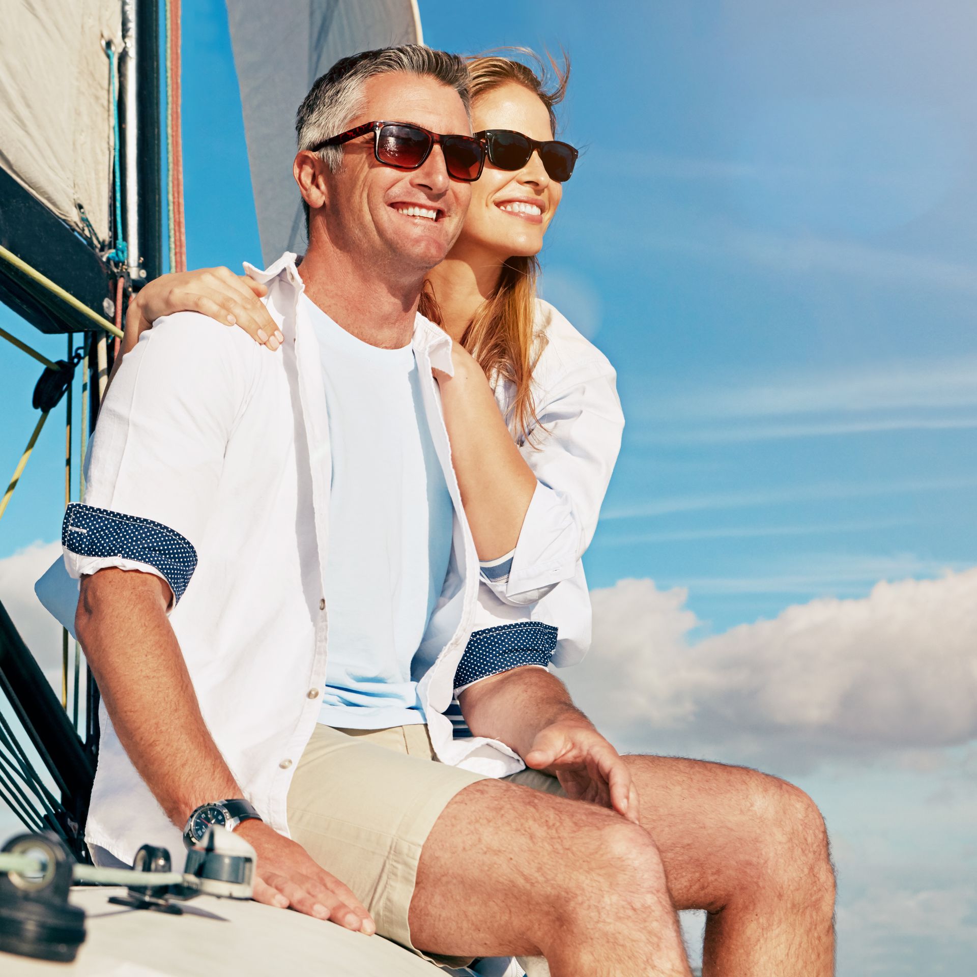 A man and woman wearing sunglasses are sitting on a sailboat