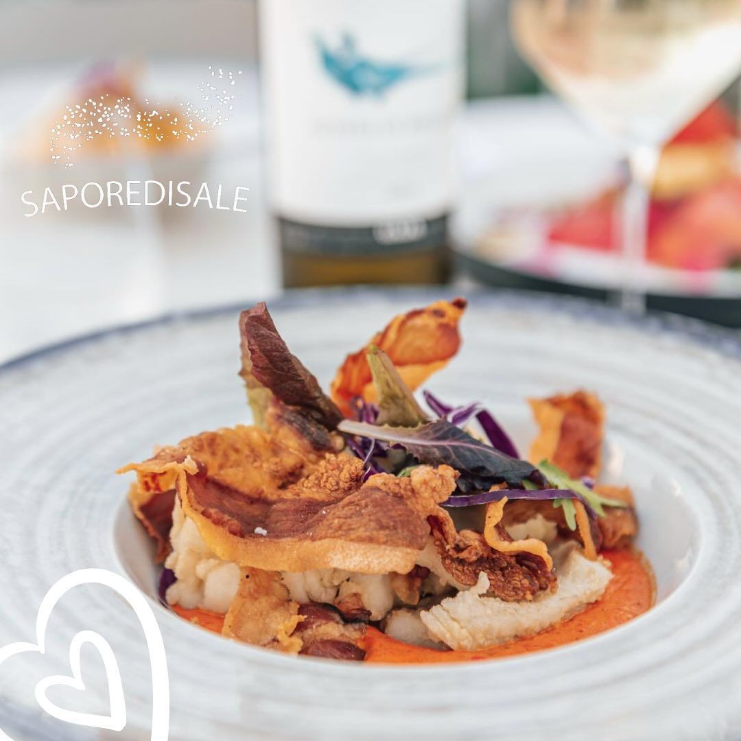 Primo piano di un piatto con del cibo, guarnito con fritture, accanto a una bottiglia di vino e un bicchiere.