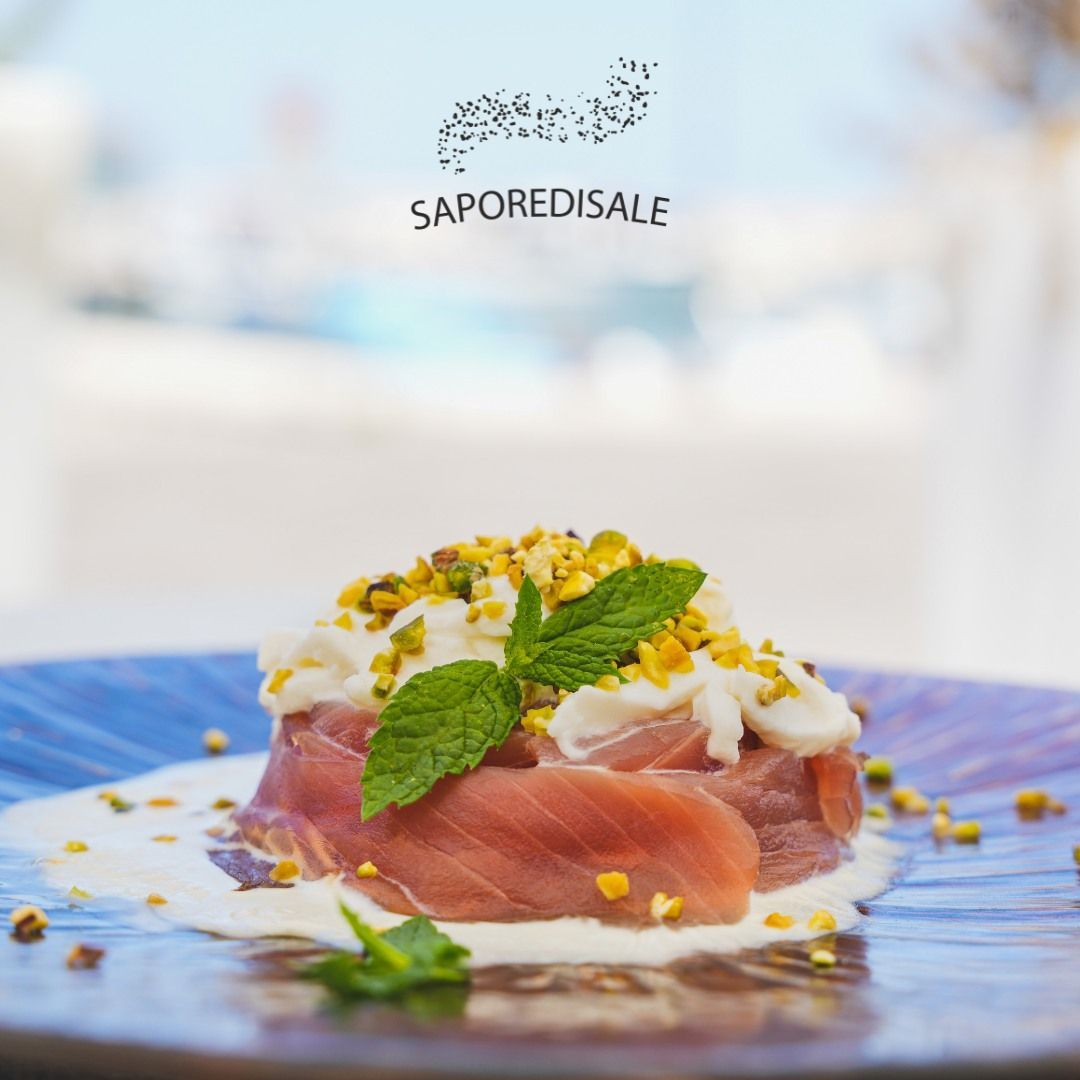 Piatto avvolto nel prosciutto con pistacchi, salsa cremosa e menta su un piatto blu.