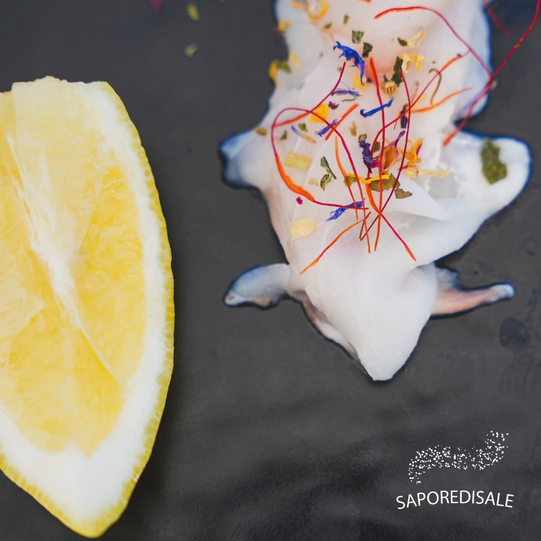 Fetta di limone accanto a un'opera d'arte culinaria bianca con fili colorati su un piatto nero.