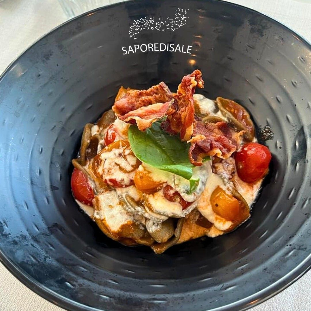 Piatto di pasta in ciotola nera, con pomodori, pancetta e basilico. Logo "SaporediSale" visibile.