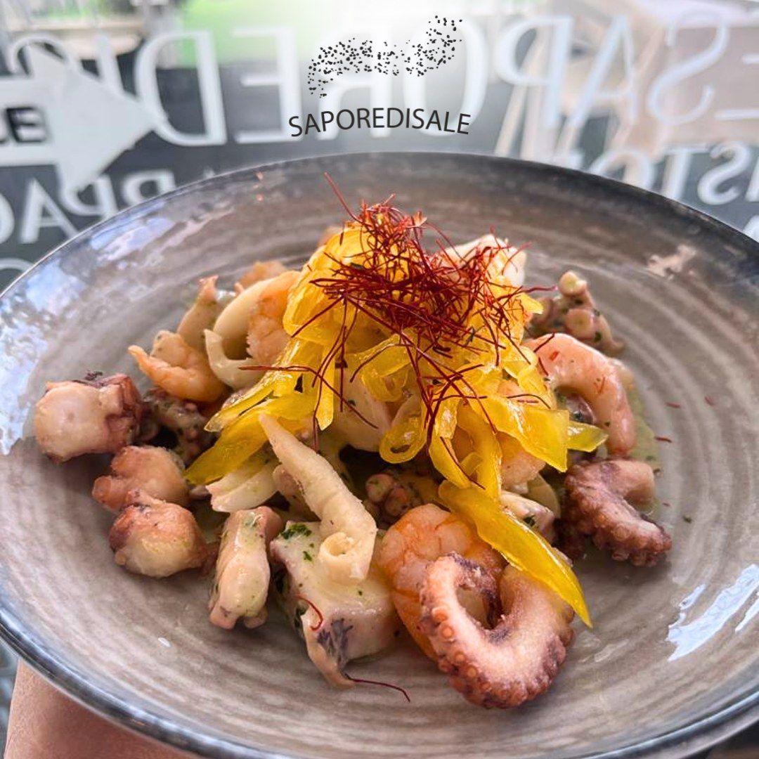 Insalata di mare con polpo, gamberi e peperoni gialli, in una ciotola grigia, all'aperto.