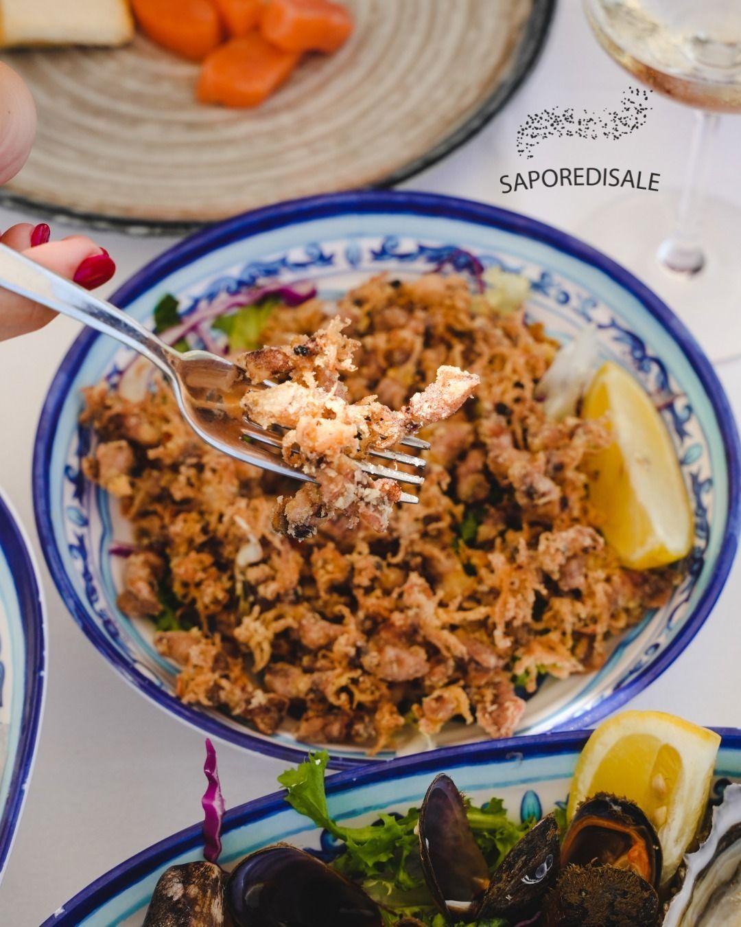 Persona che mangia con la forchetta pesce fritto da un piatto decorato con motivi blu e bianchi, guarnito con limone.
