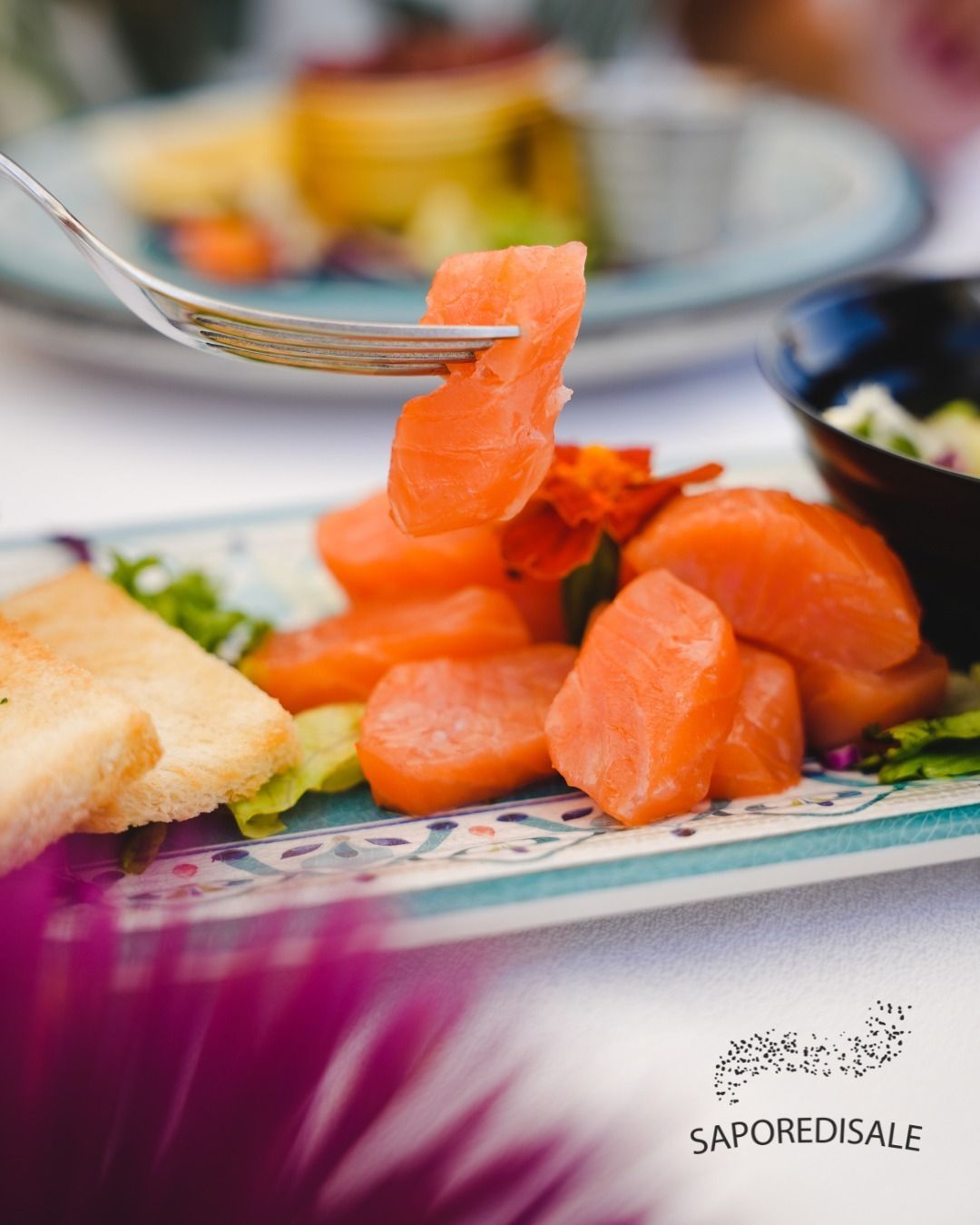 Salmone affumicato su un piatto decorativo con pane tostato, una forchetta che solleva una fetta.