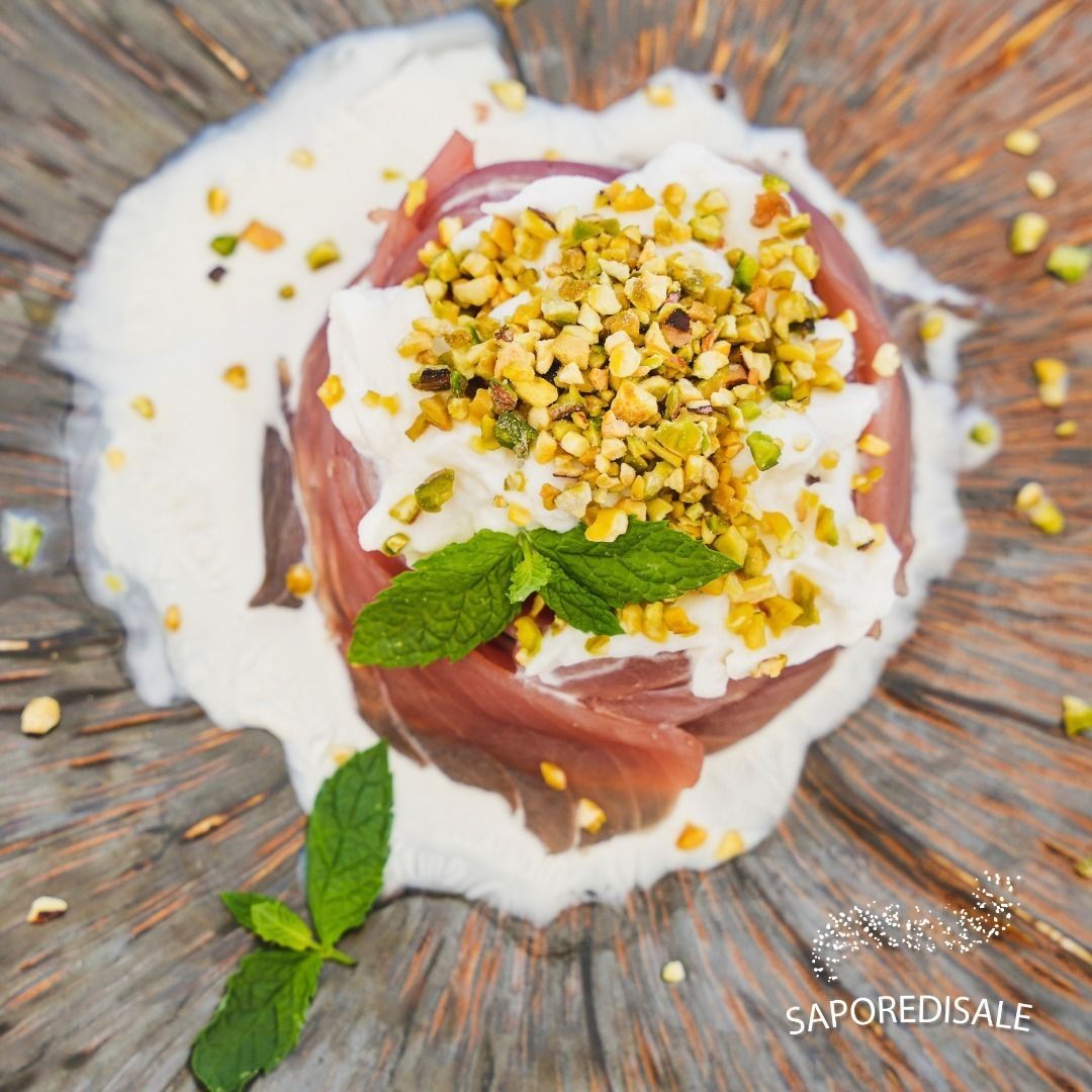 Piatto di prosciutto: disposto su un piatto con salsa cremosa, guarnito con pistacchi e menta.