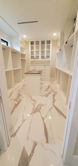 A walk in closet with marble floors and white cabinets.