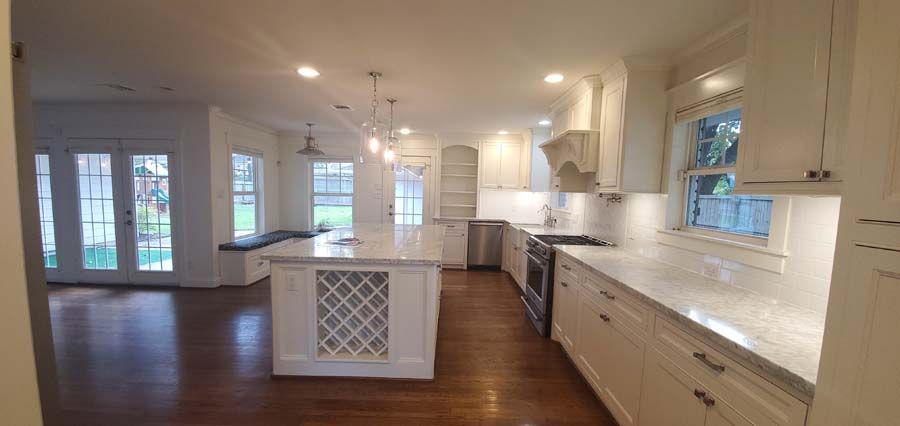 A kitchen with white cabinets , granite counter tops , stainless steel appliances and a large island.