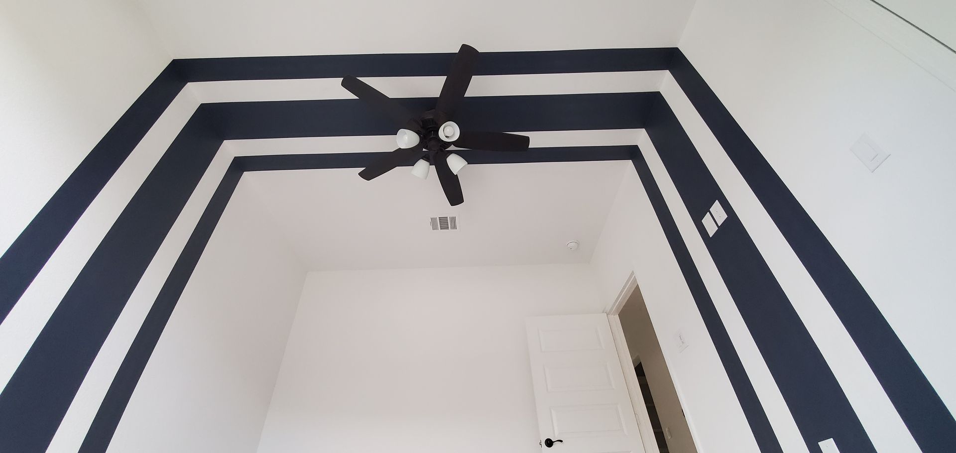 A black and white striped wall with a ceiling fan