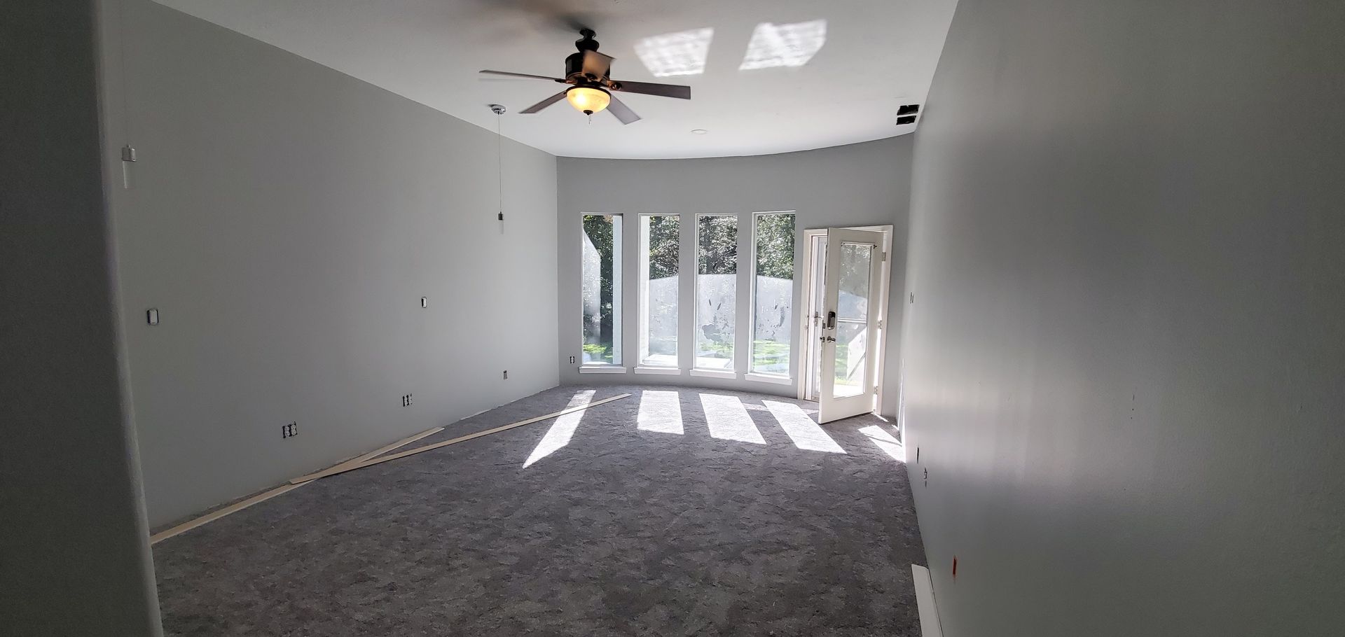 An empty living room with a ceiling fan and sliding glass doors.