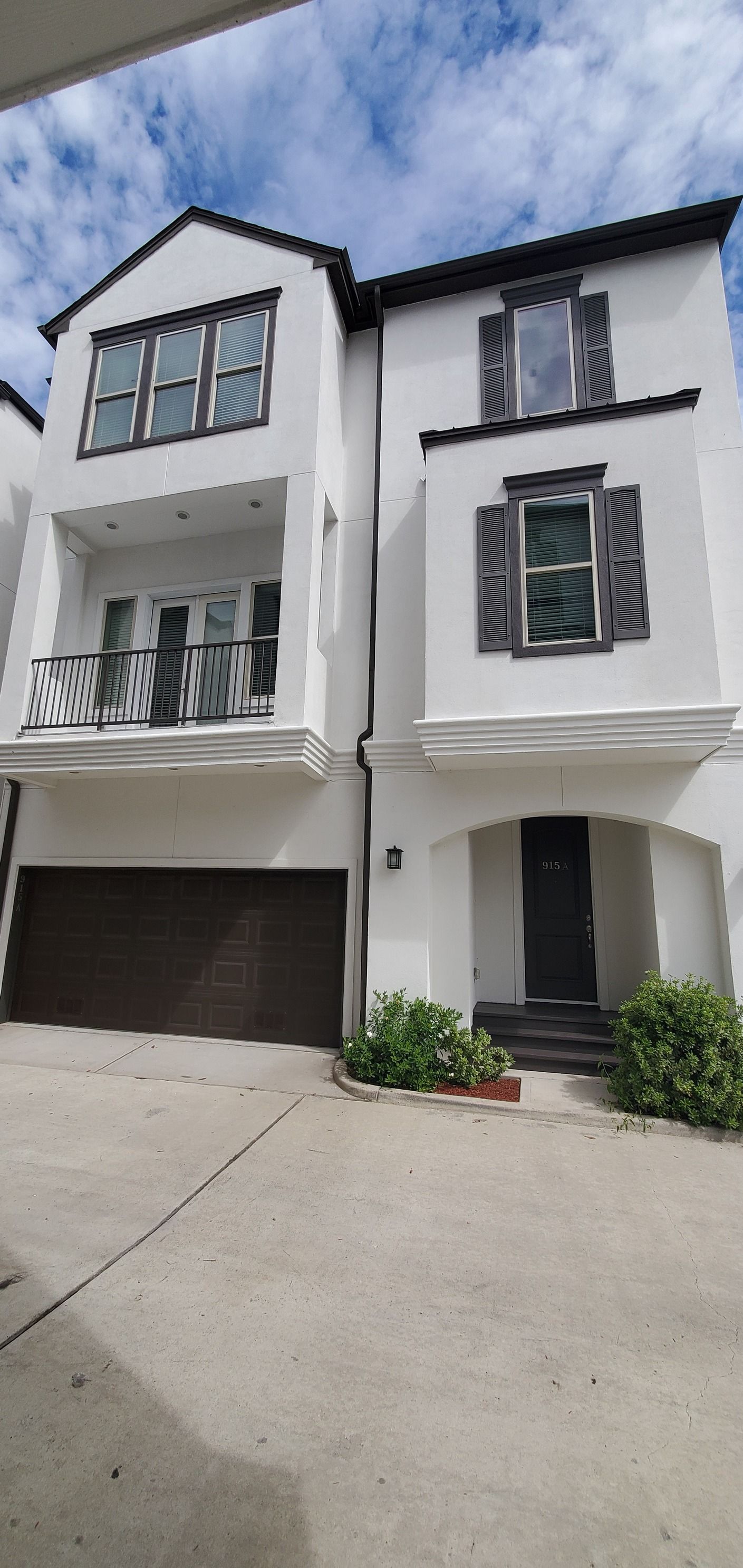A white house with a brown garage door and a balcony.