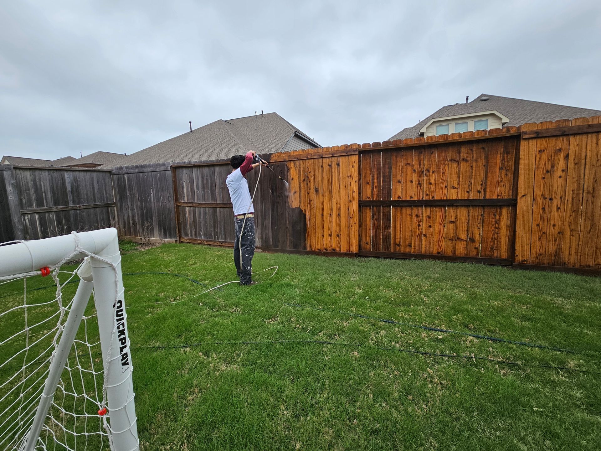 A man is painting a wooden fence in a backyard.