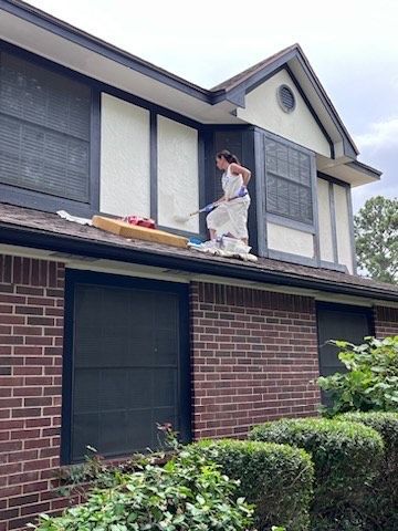A man is painting the side of a brick house.