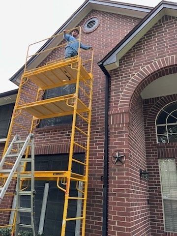 A man is standing on a scaffolding in front of a brick house.