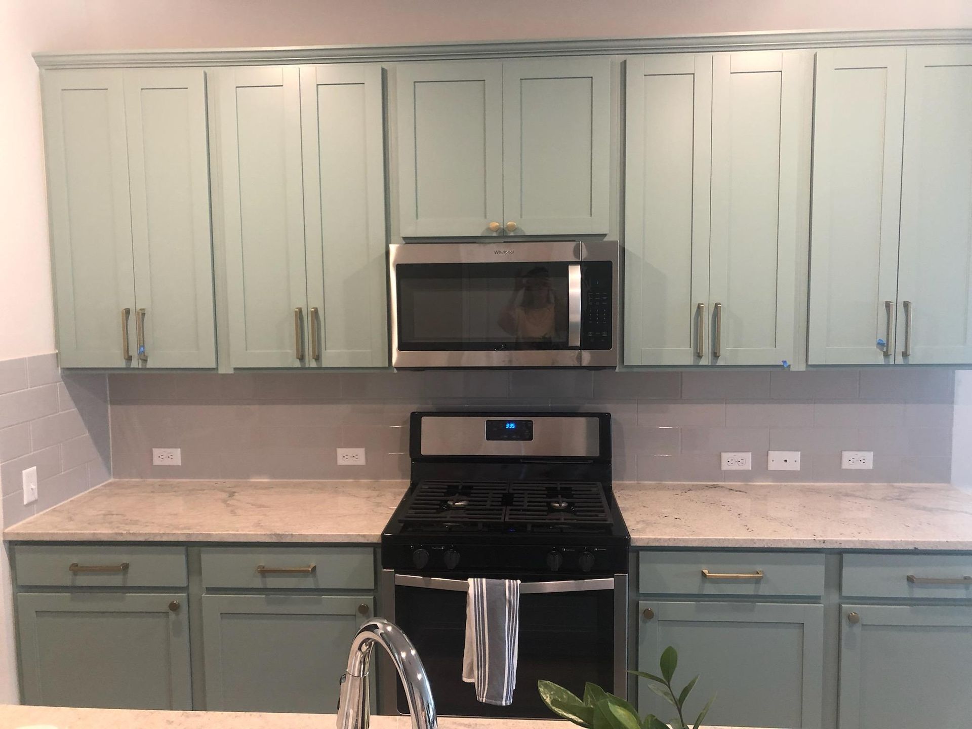 A kitchen with blue cabinets , a stove , microwave and sink.