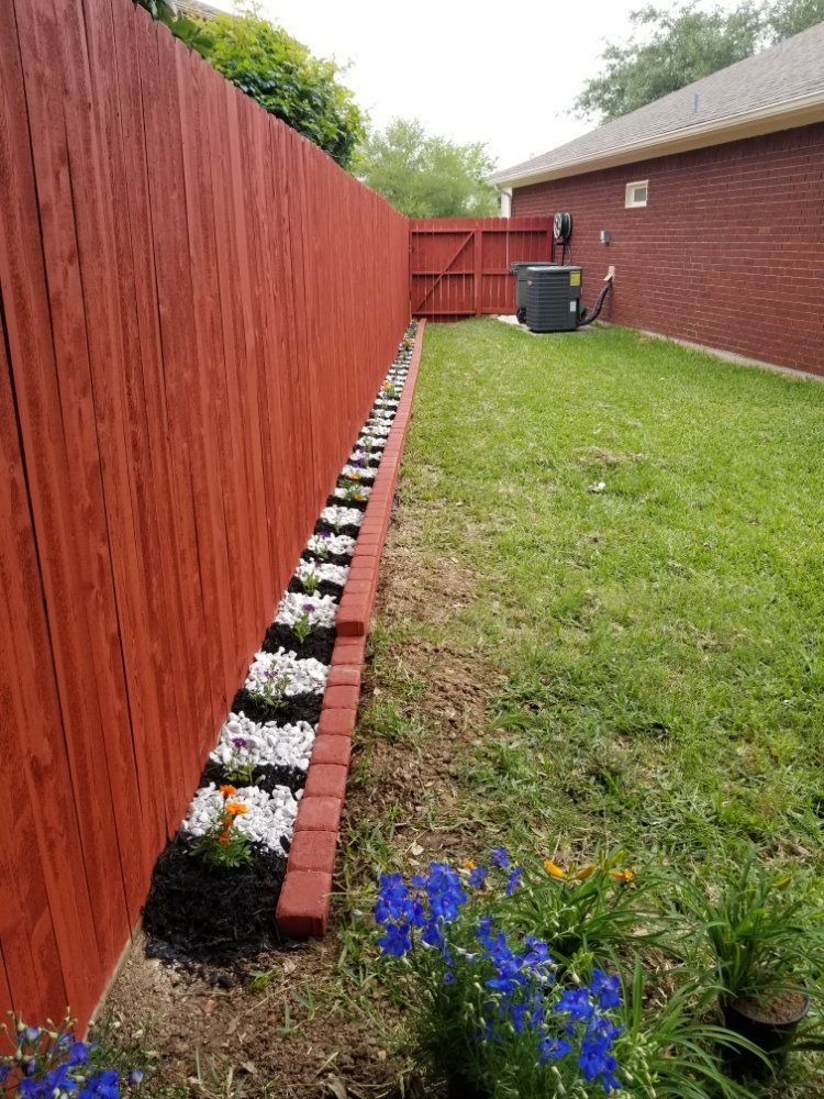 A red fence surrounds a lush green yard with flowers and rocks.