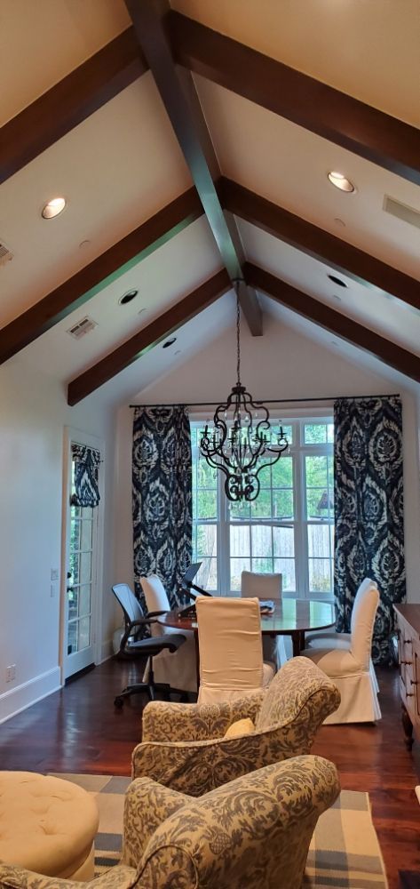 A living room with a vaulted ceiling , chairs , a table and a chandelier.
