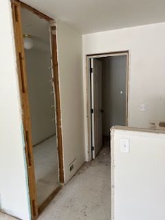 Interior view of a hallway with two doorways. The left door frame lacks a door. Right doorway has a closed door.