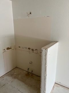 Empty corner space with drywall and plumbing. Bare floor and wall.