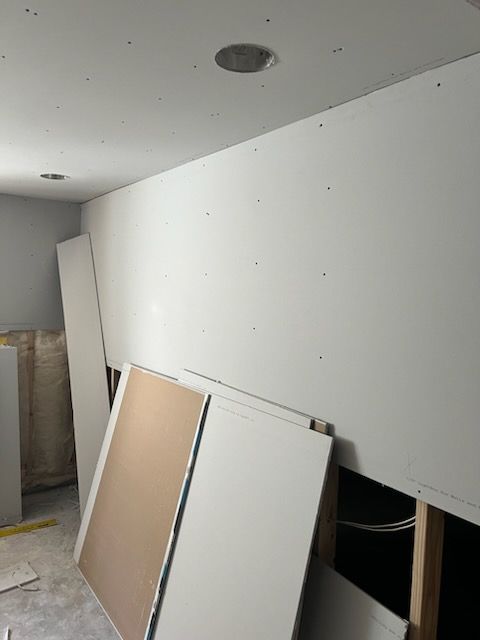 Drywall being installed in a room, with stacked sheets and recessed lighting.