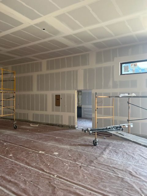 Interior under construction; drywall installed on walls and ceiling, covered floor, scaffolding, and a doorway.