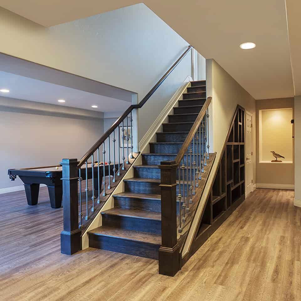 Staircase with dark wood railing and spindles, leading to a basement game room with a pool table and built-in shelving.