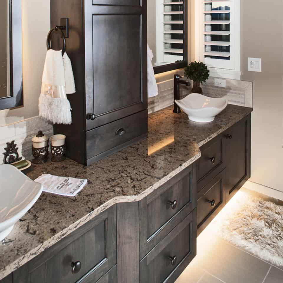 Dark gray bathroom vanity with countertop, sinks, drawers, towel rack, and rug.