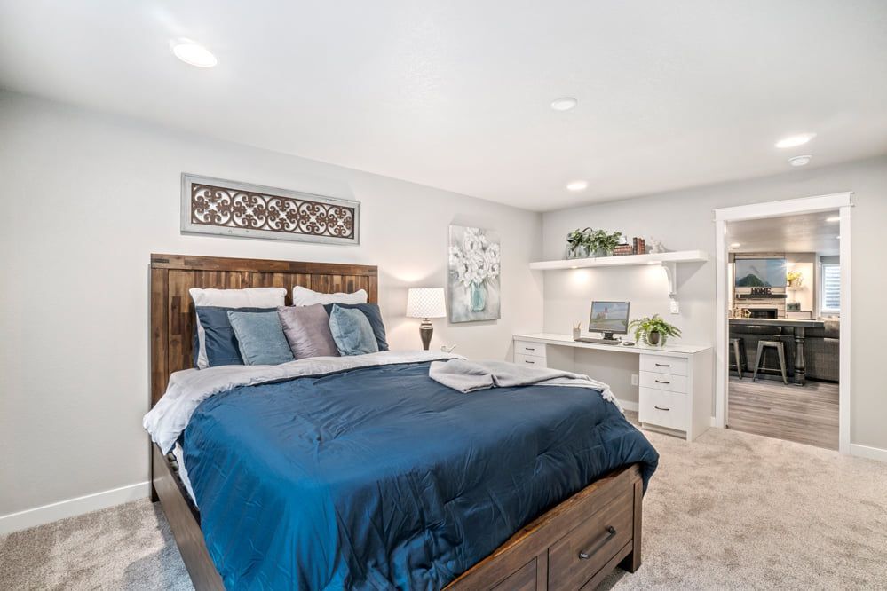 Bedroom with bed, desk, and a view into the kitchen. Bedding is blue, walls are light gray.