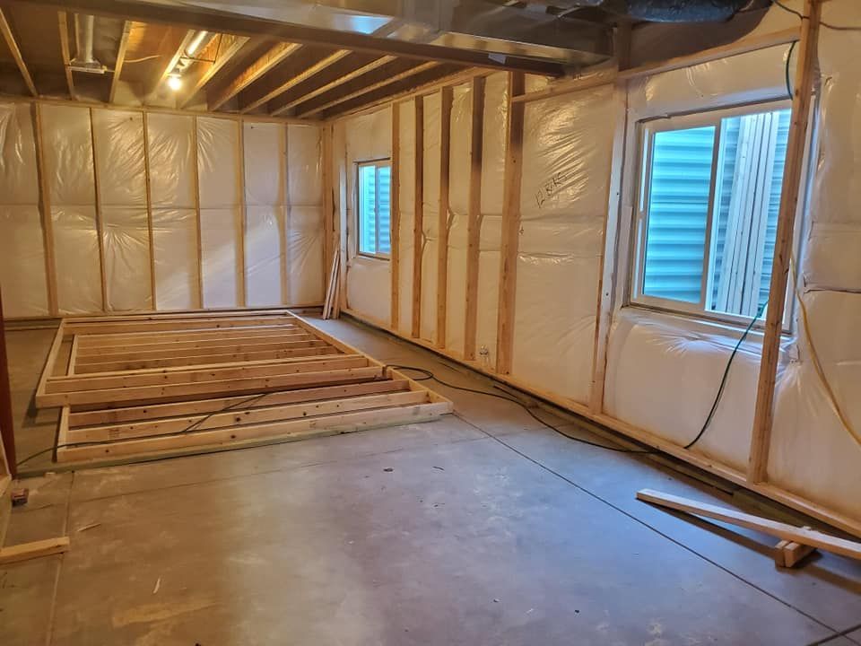 Basement under construction: wooden framing, insulation, windows, and a partially built floor.