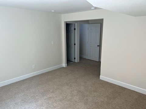 Empty room with beige carpet, white walls, and doorway leading to two doors.