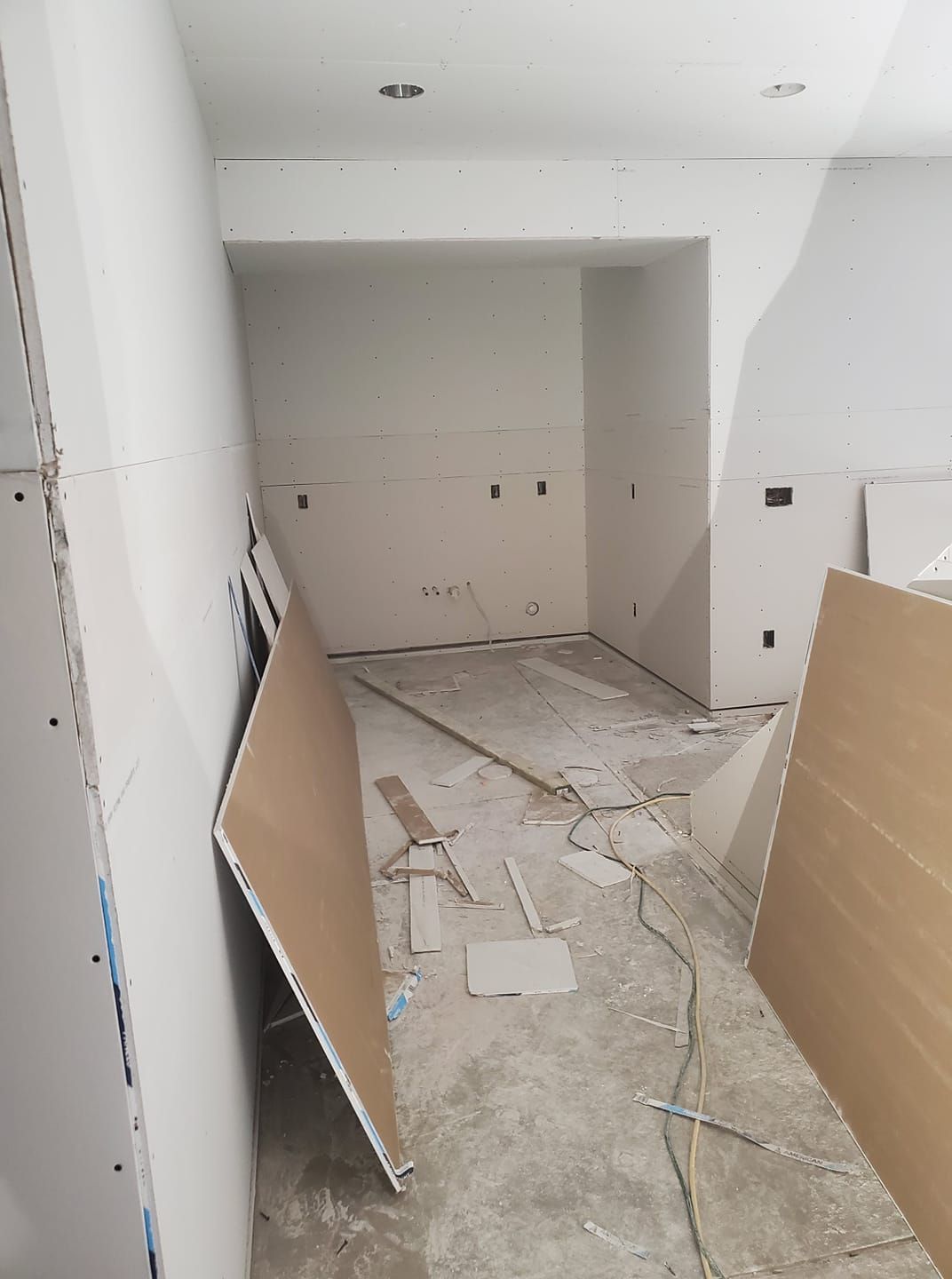 Interior room under construction, drywall installed, unfinished floor, electrical wires, and materials scattered.