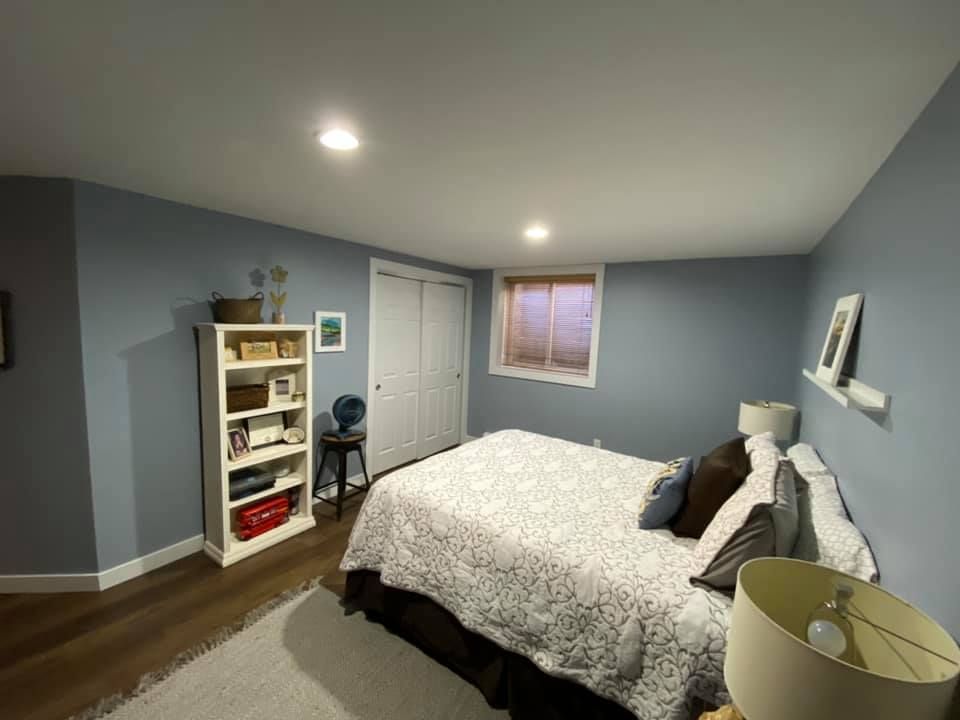 Bedroom with blue walls, bed, bookshelf, window, closet, and wood flooring.