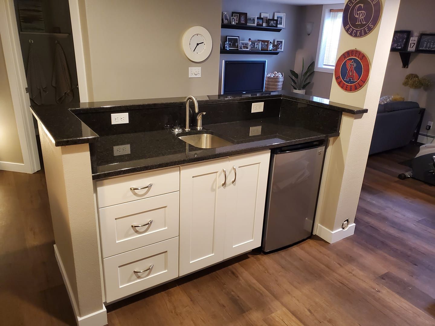 Bar with black countertop, white cabinets, stainless steel fridge, and silver faucet.