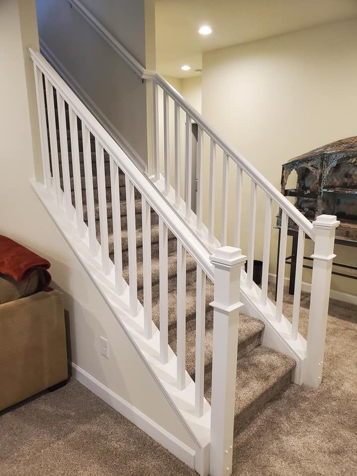White stair railing with vertical balusters, tan carpet, and stairs leading downward.