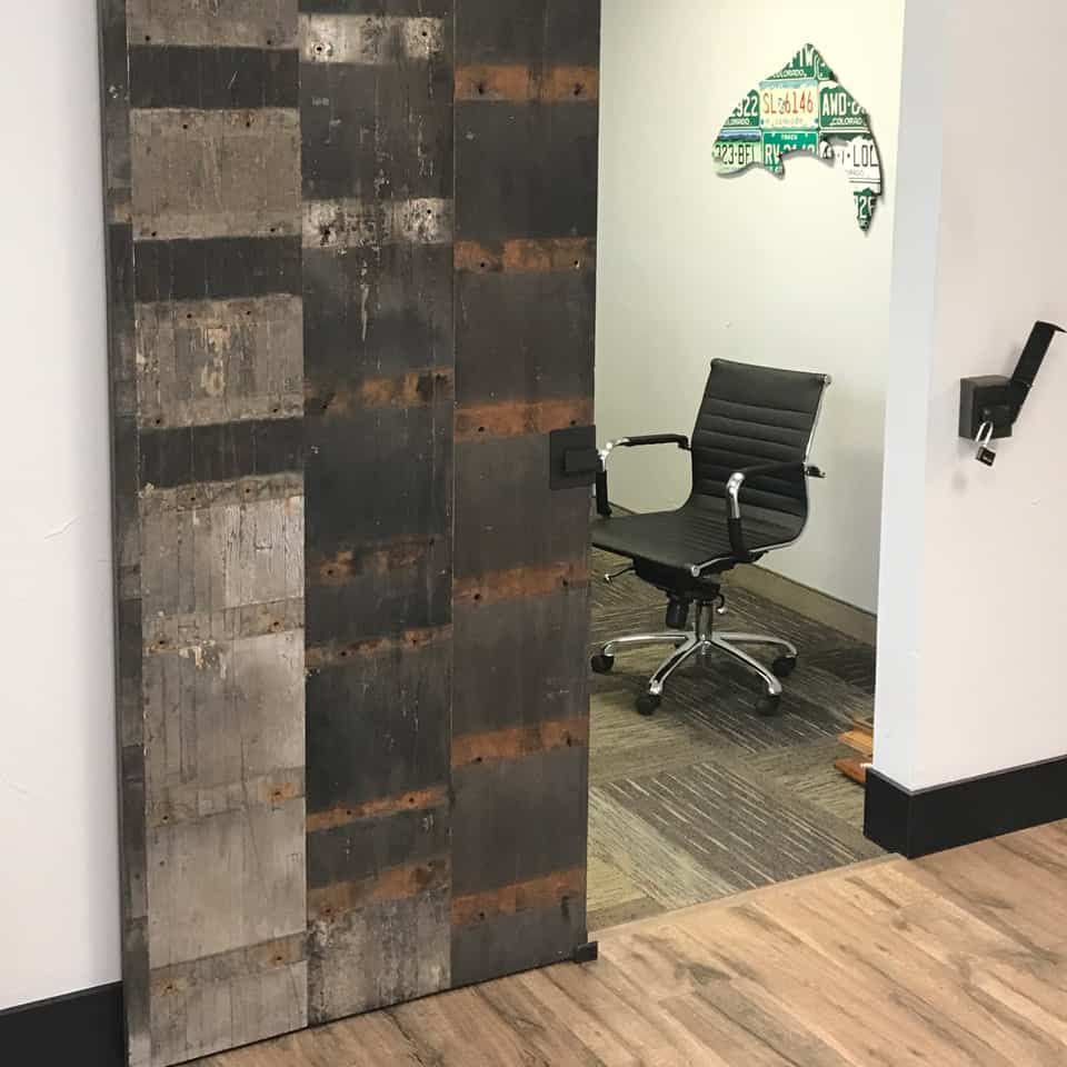 Barn door entrance to office with black chair, art, and wood floors.