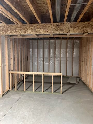 Unfinished basement with framed walls, ceiling joists, insulation, and a low framed structure on the concrete floor.