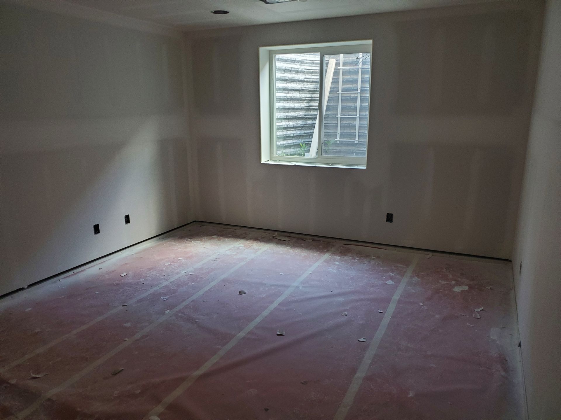 Empty room with unfinished drywall, window, and floor covered in protective sheeting.